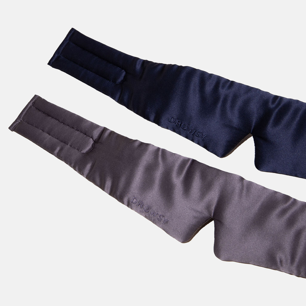 The drowsysleepco Lovers Pack features two luxury silk blackout eye masks in navy blue and dark gray with padded, contoured designs, subtle DROWSY branding, curved shapes, and velcro straps—shown laid flat on a light background.