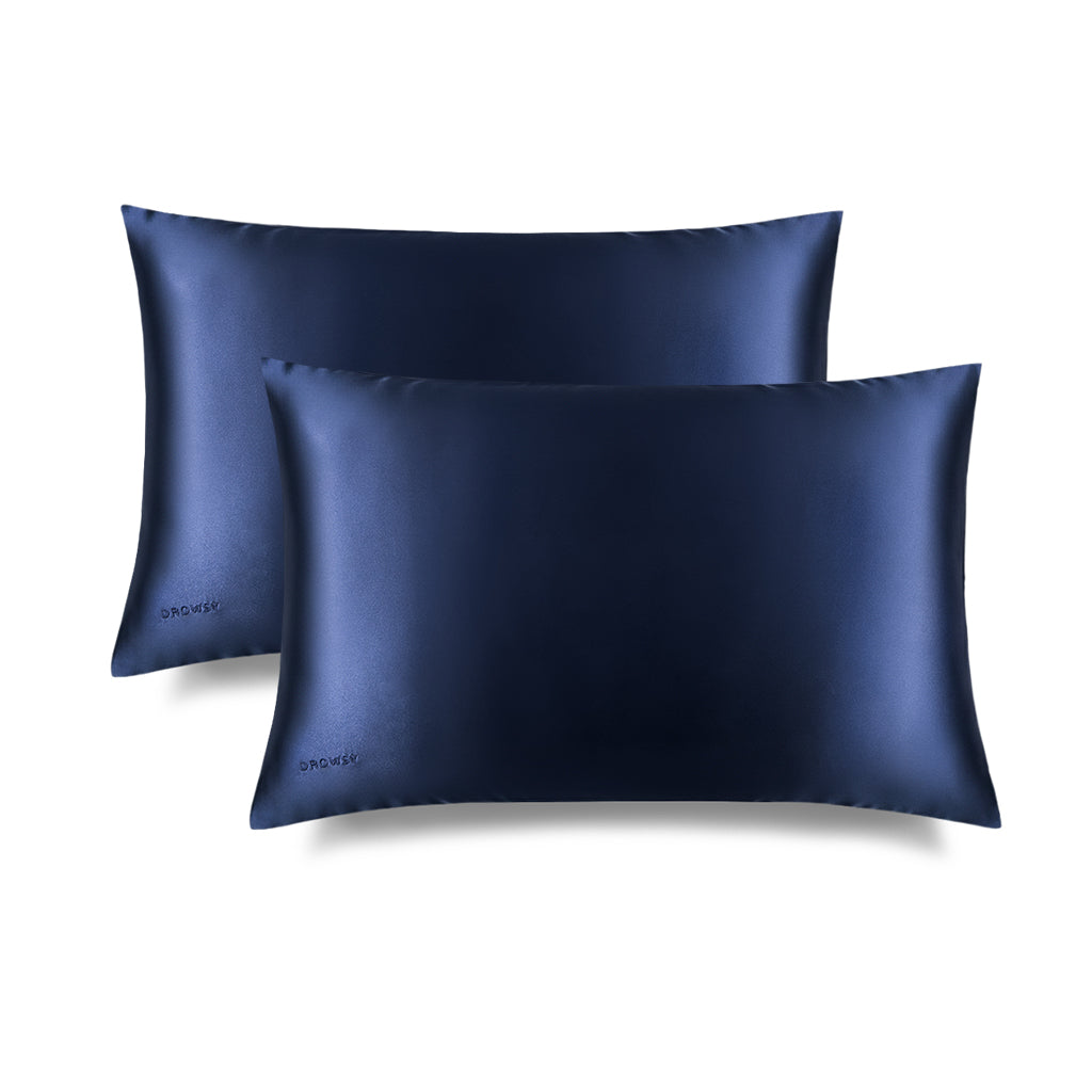 Two drowsysleepco Midnight Blue Silk Pillowcases with a smooth, shiny finish overlap on a white backdrop—ideal for protecting your skin and hair as you sleep.