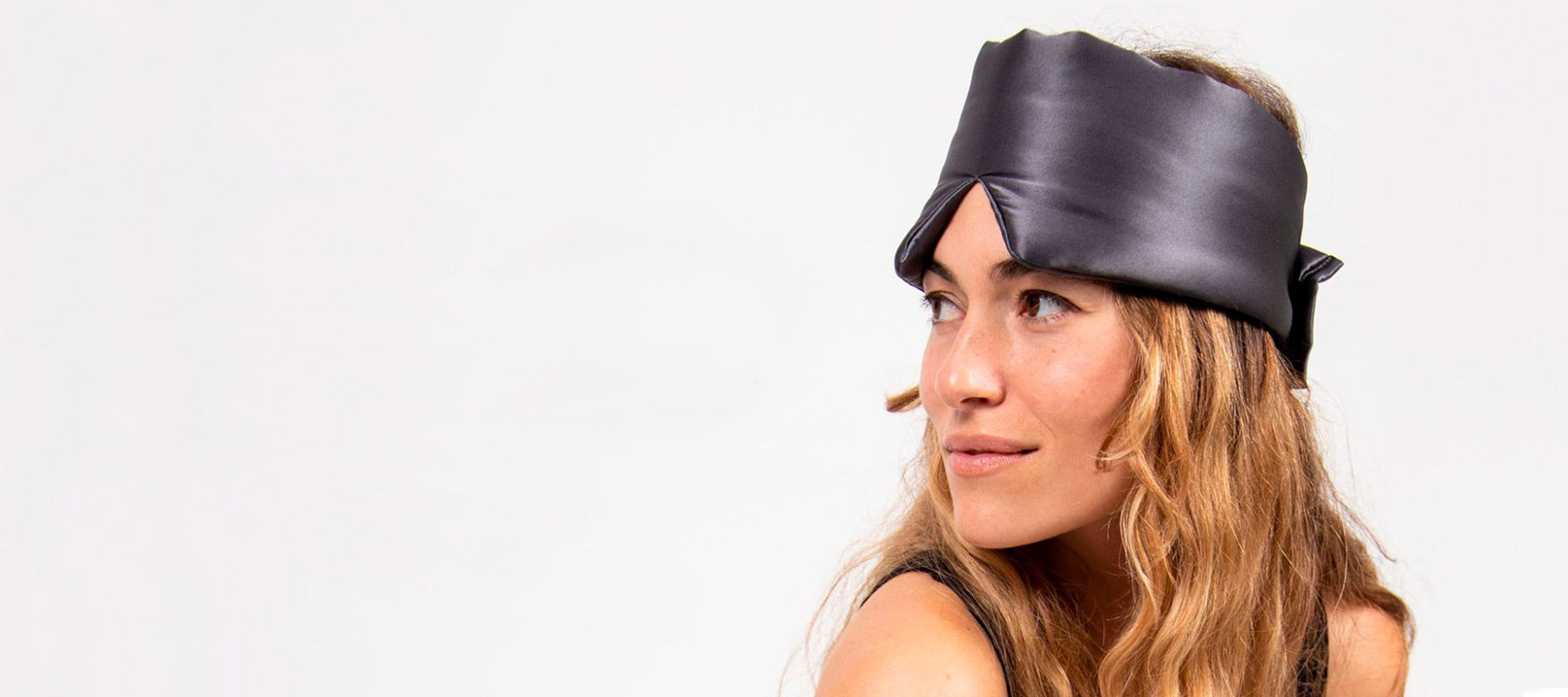 A woman with long, wavy hair wearing a shiny black headscarf looks off to the side against a plain white background.