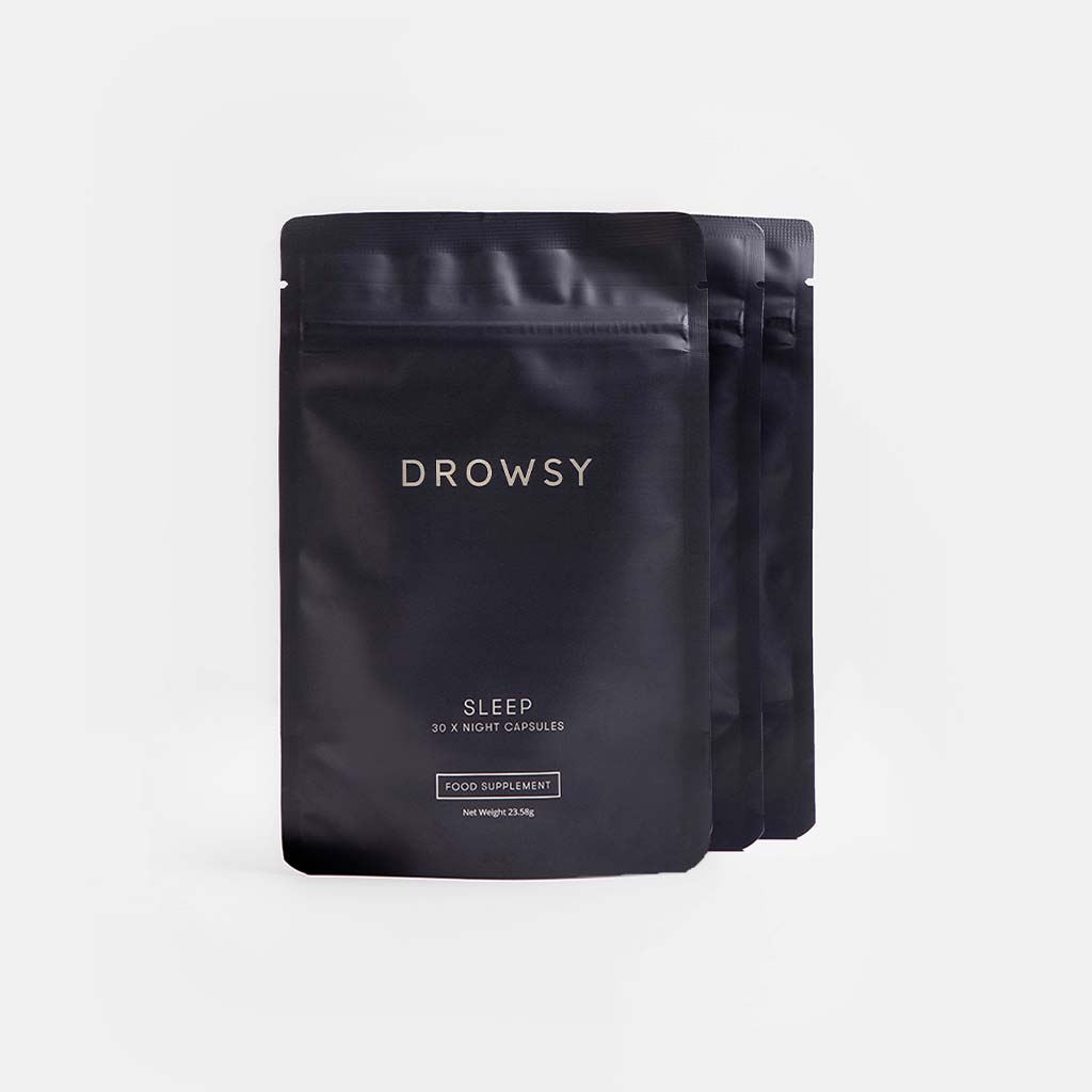 Three black resealable pouches of drowsysleepco’s Sleep Supplement Subscription are arranged in a row on a light gray background. The minimalist packaging features simple white text and contains 30 Night Capsules each.