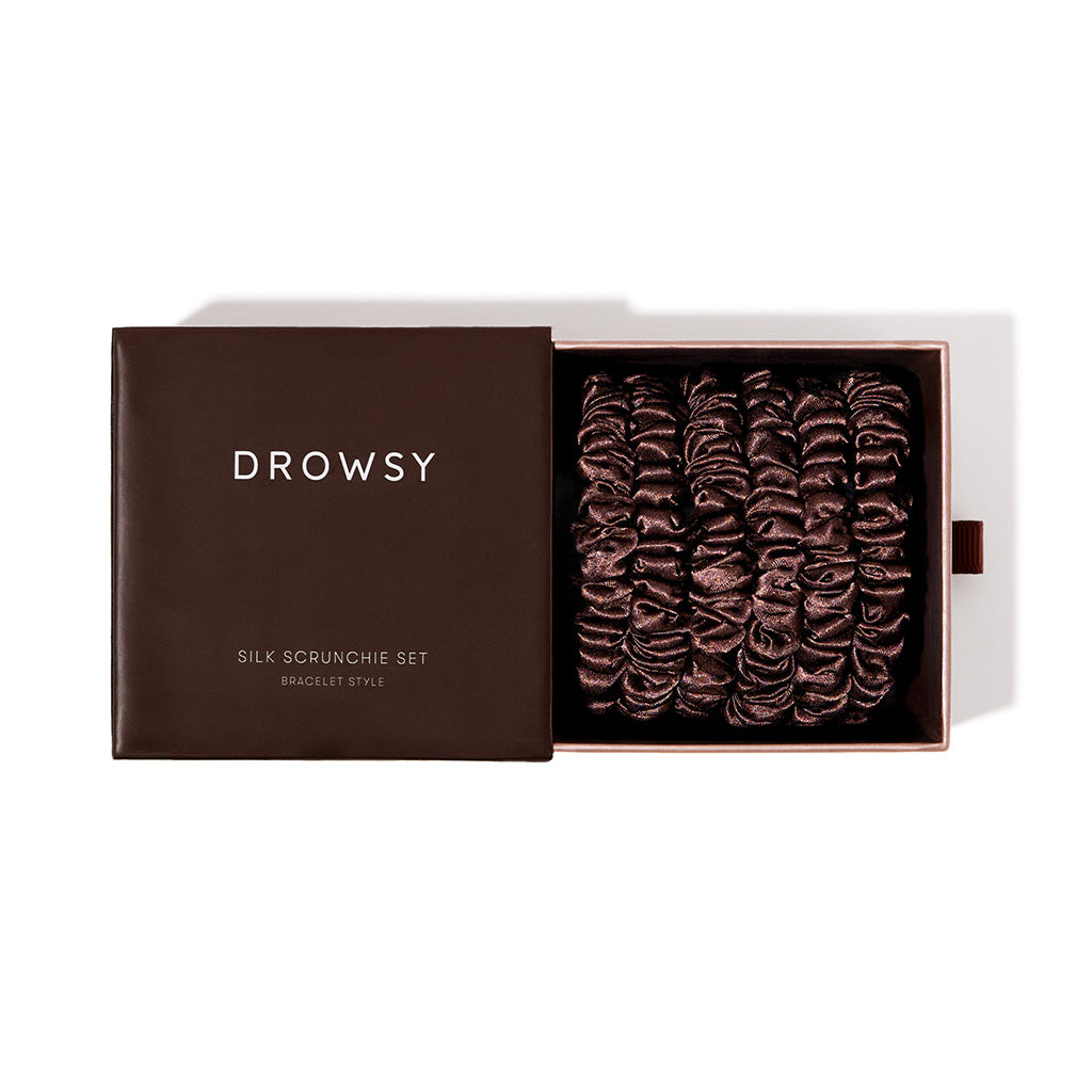 An open brown box labeled drowsysleepco Skinny Scrunchie Set - Cocoa Glow reveals several dark brown 22 momme silk scrunchies, neatly arranged for hair health and stylish comfort.