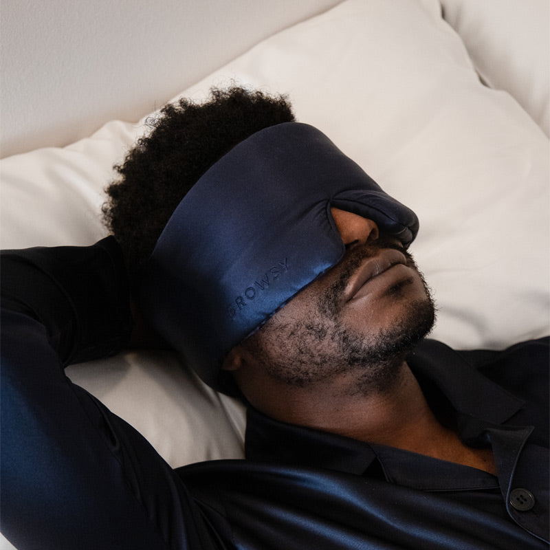 A man relaxes with a drowsysleepco 2-Pack Sleep Mask in Midnight Blue, resting comfortably on a white pillow—ideal for restful nights or as a thoughtful Valentine’s gift.