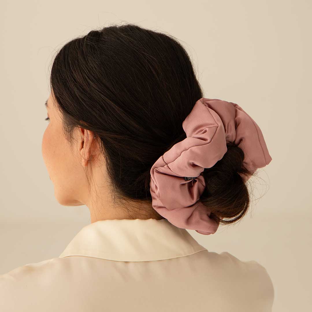 A woman with dark hair in a low bun, styled with the Damask Rose - Padded Scrunchie by drowsysleepco, wears a cream blouse and stands against a light background.