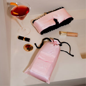 The drowsysleepco Sleep and the City - Pink & Black Sleep Mask + Pouch rests on a cream surface next to chic accessories—a stylish way to improve skin and elevate your night routine.