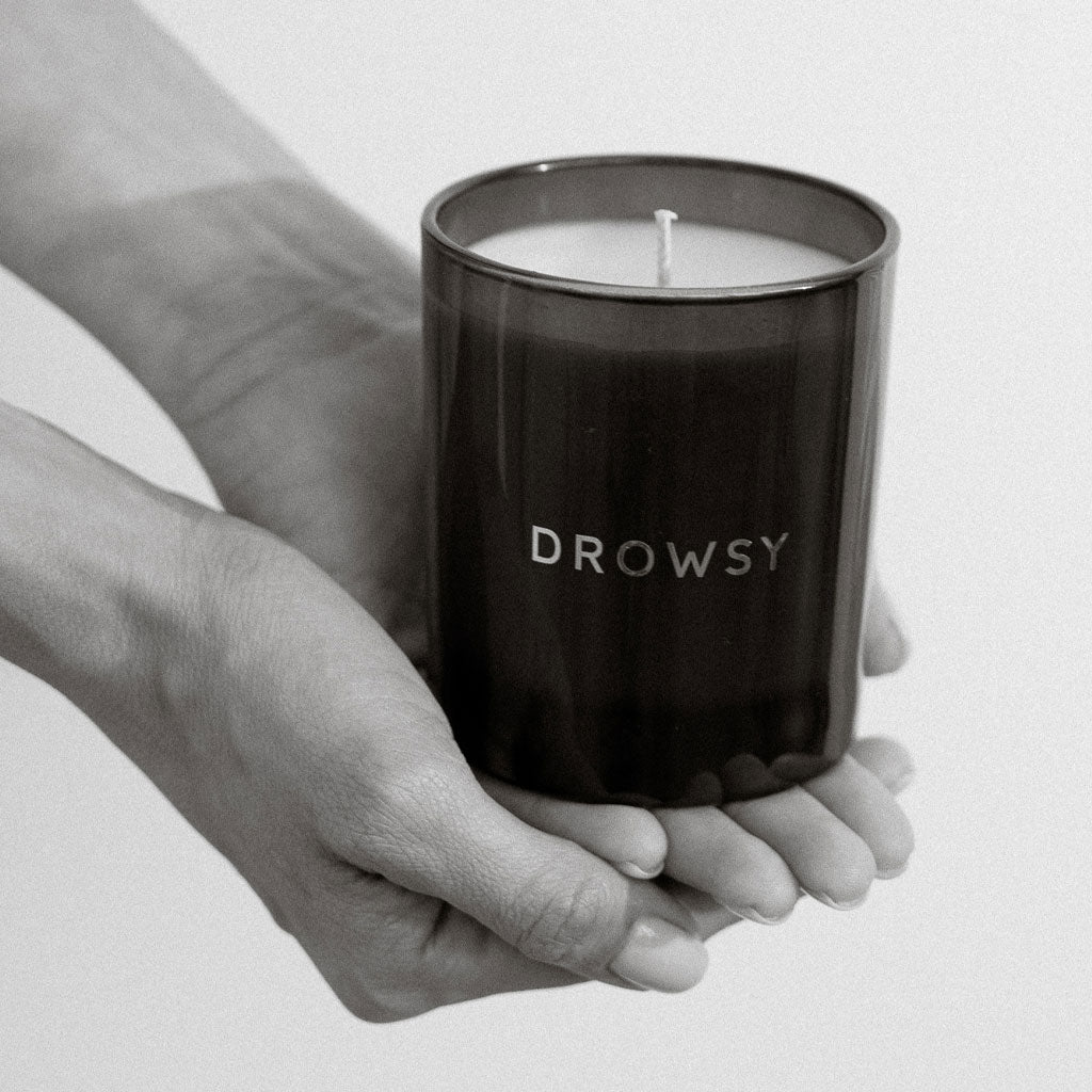 A person holds a Sleep Ritual Candle 220g by drowsysleepco, housed in a dark glass jar, against a plain background.