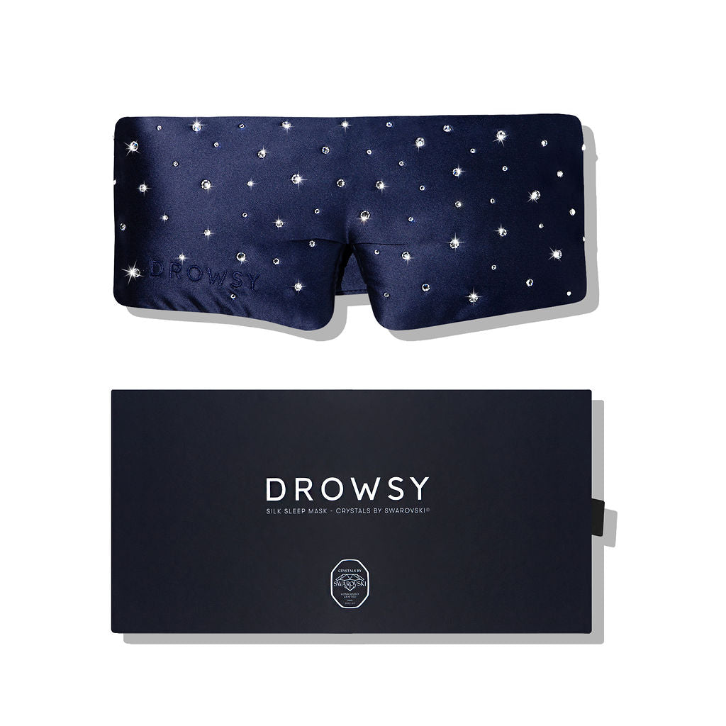A navy blue drowsysleepco Silk Sleep Mask Crystals by Swarovski® rests on a matching dark box, combining luxury silk with sparkling Swarovski® accents for a premium blackout sleep mask experience.