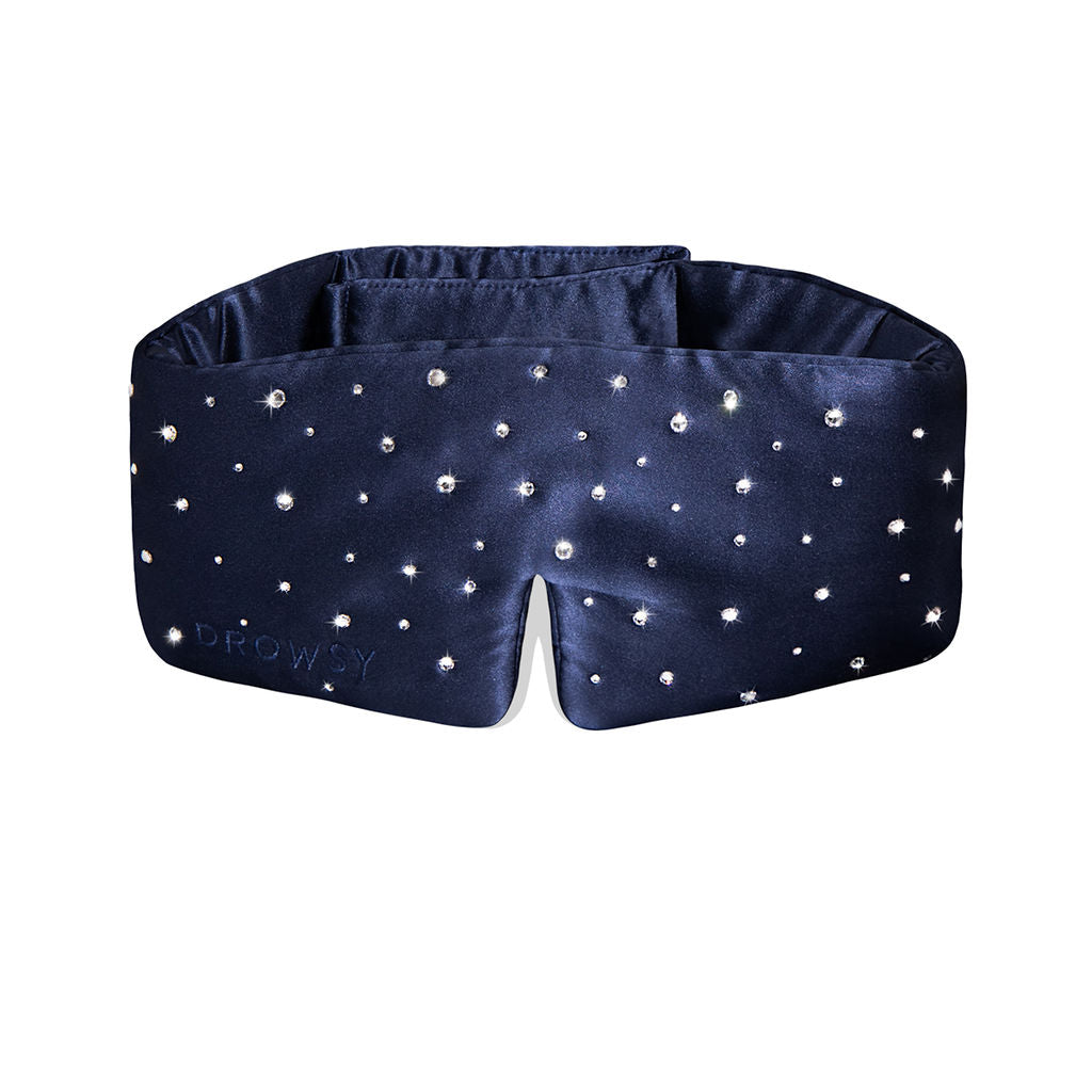 The Silk Sleep Mask Crystals by Swarovski® from drowsysleepco features navy blue silk, sparkling Swarovski® crystals for a starry effect, soft padding, blackout coverage, and DROWSY subtly embossed on the fabric.