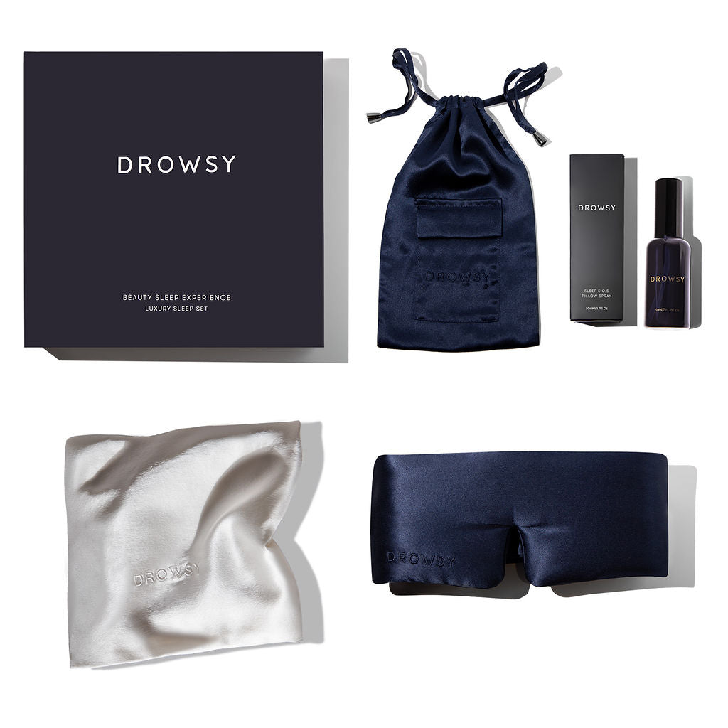 The drowsysleepco Beauty Sleep Experience includes a dark gift box, navy drawstring pouch, black deep sleep pillow spray bottle, mulberry silk pillowcase, and a navy silk sleep mask, all displayed on a white background.