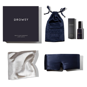 The drowsysleepco Beauty Sleep Experience includes a dark gift box, navy drawstring pouch, black deep sleep pillow spray bottle, mulberry silk pillowcase, and a navy silk sleep mask, all displayed on a white background.