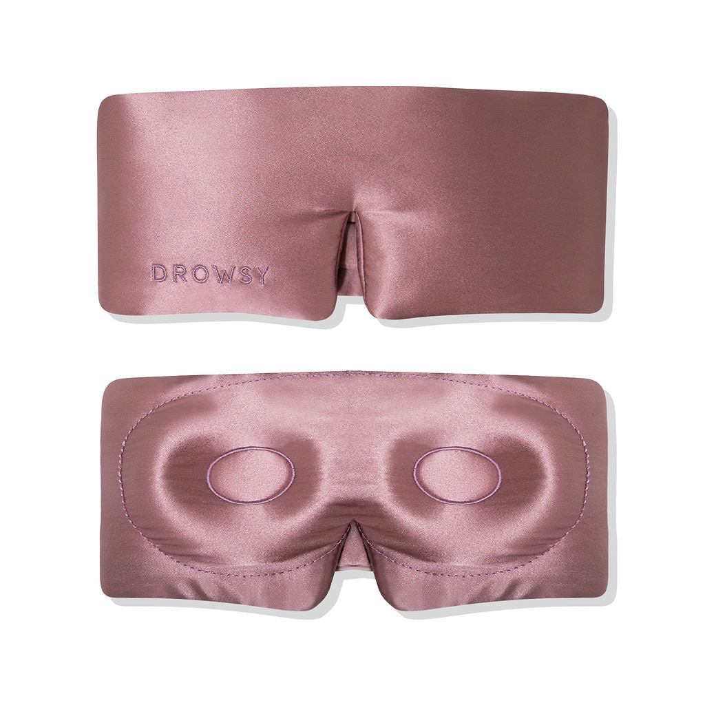 Two views of a pink satin sleep mask: the top view shows DROWSY embroidered, while the bottom view shows the mask’s interior with stitched eye cushions for comfort.