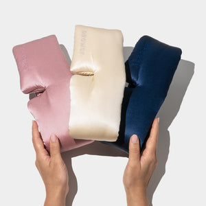 Two hands hold drowsysleepco’s Besties Pack: three luxury mulberry silk sleep masks in pink, cream, and navy blue, side by side on a white background. Each padded blackout eye mask offers ultimate comfort.