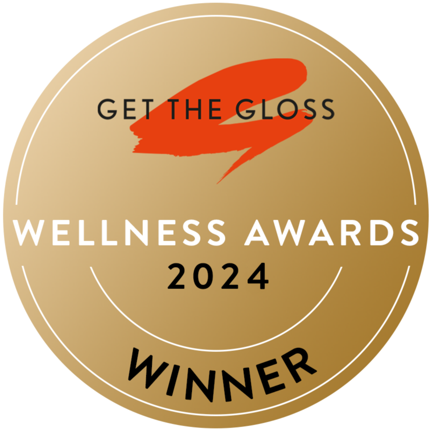 A gold circular badge with “Get The Gloss Wellness Awards 2024 Winner” written on it and a red brushstroke design above the text.