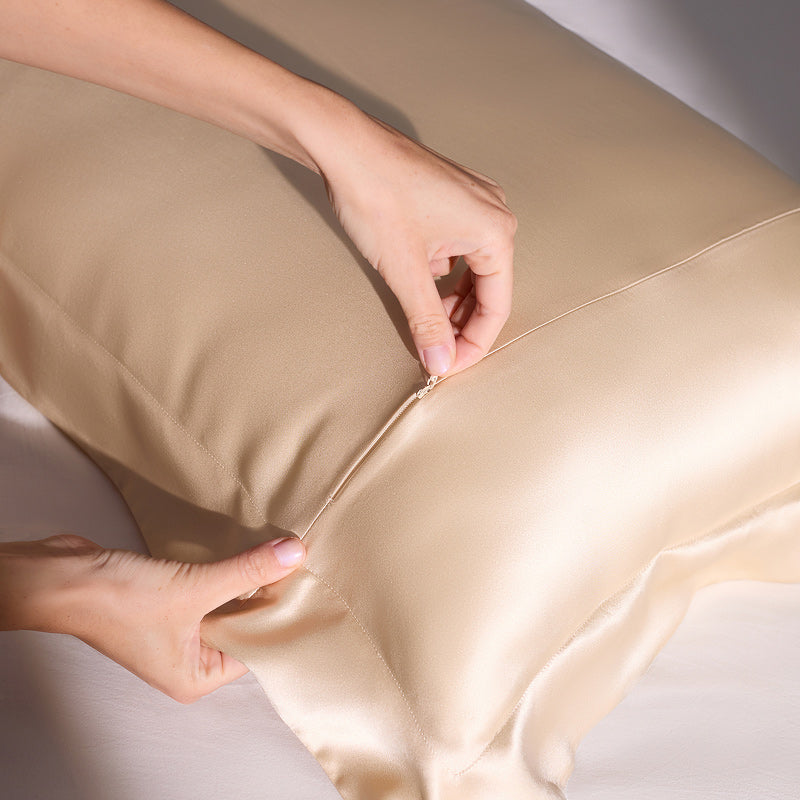 A person is zipping up the Hyalo Pillowcase - Champagne Gold by us.drowsysleepco onto a pillow, with both hands visible against a white surface.