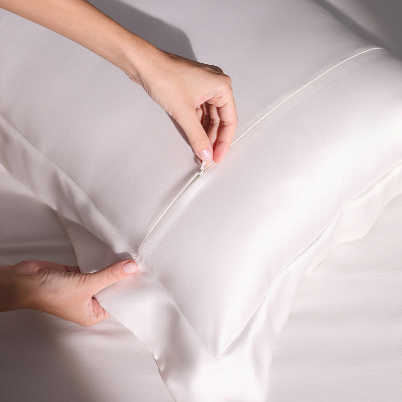 A person’s hands are shown zipping up the us.drowsysleepco Hyalo Pillowcase - Akoya Pearl onto a pillow, with both the pillow and bedding appearing smooth and clean.