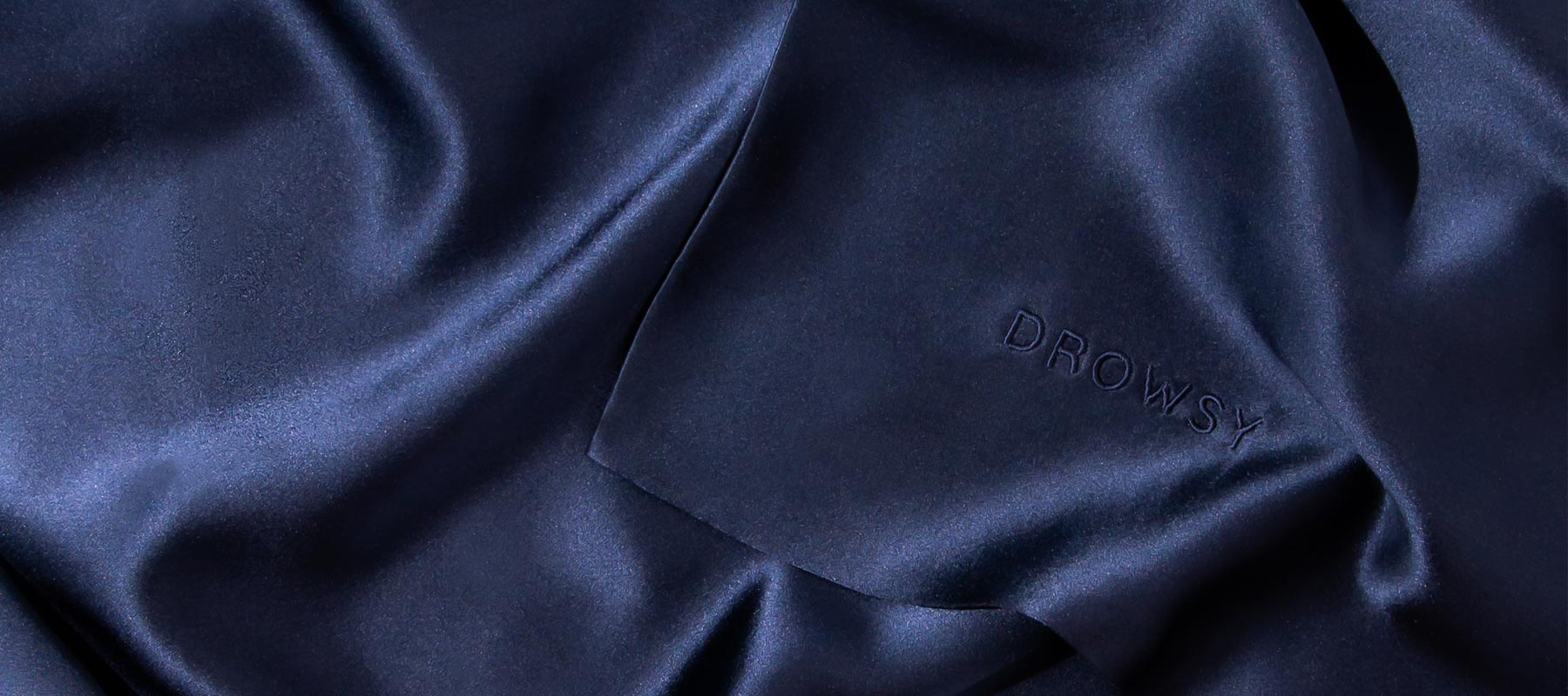 Smooth, dark navy blue silk fabric with subtle folds and the word DROWSY embossed on the surface.