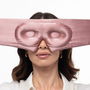 A woman wearing a wide, mauve-colored Pride & Prejudice - Sage + English Rose Eyelash Protecting Masks mulberry silk sleep mask over her eyes.