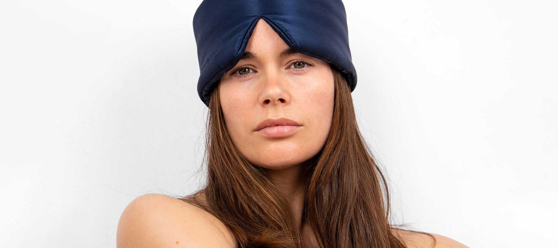 A woman with long brown hair wears a dark blue satin head wrap and looks directly at the camera with a neutral expression, set against a plain white background.