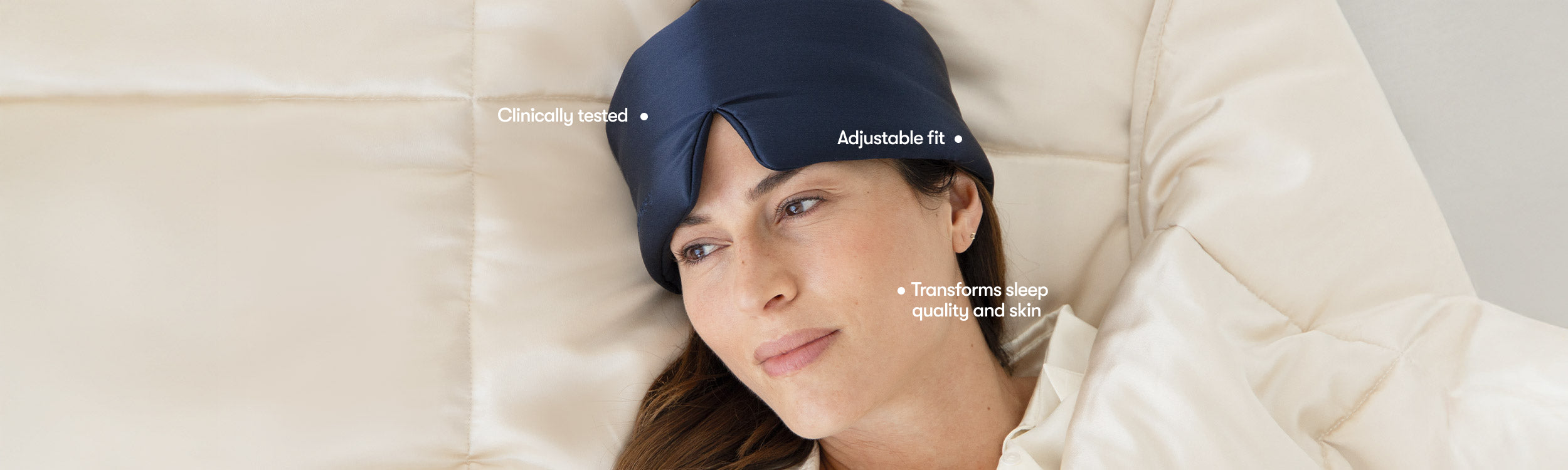 A woman lies on a cream-colored pillow and blanket, wearing a navy blue sleep mask. Text labels highlight features: Clinically tested, Adjustable fit, and Transforms sleep quality and skin.