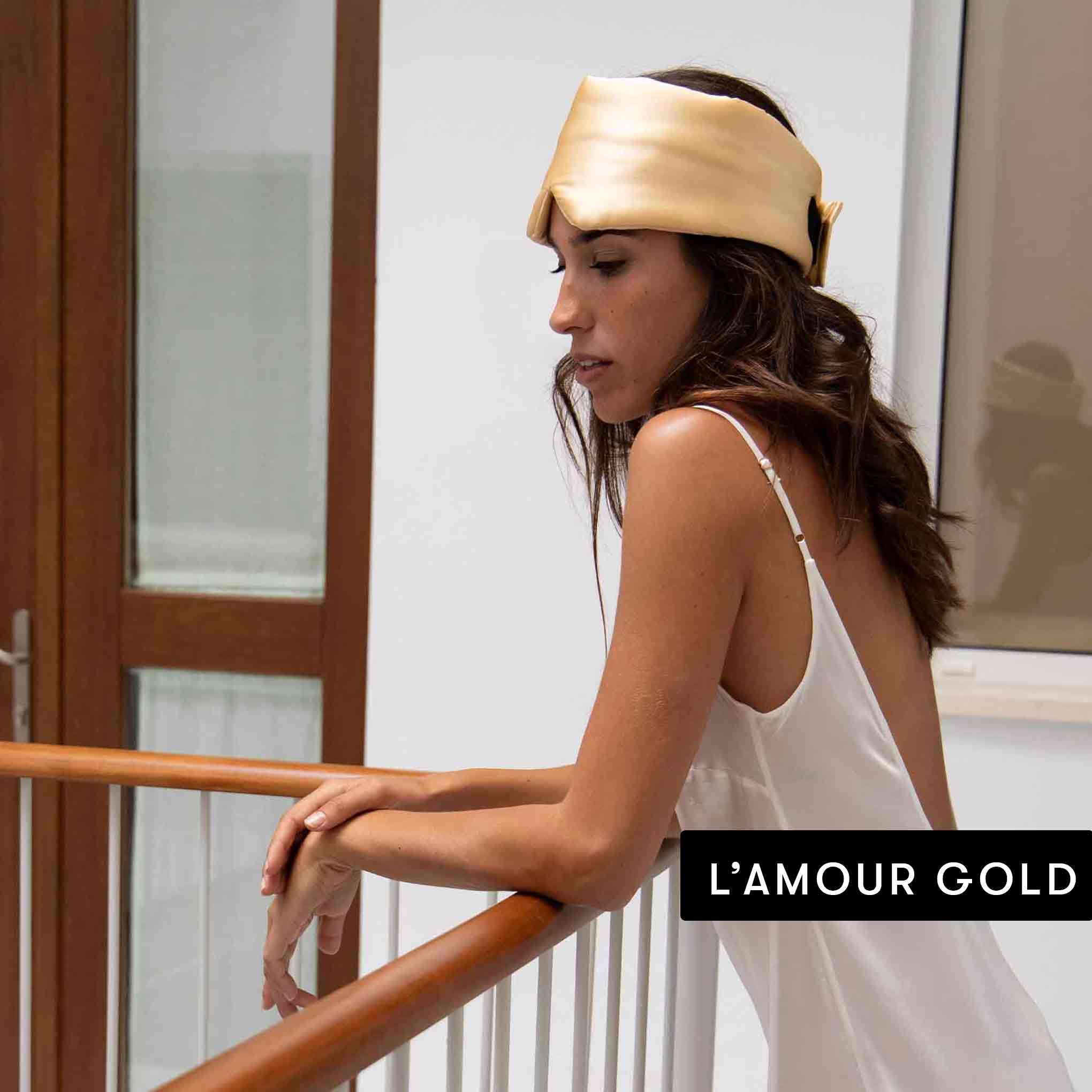 A woman in a white satin dress leans on a railing indoors, wearing a shiny gold satin headband. In the bottom right corner, Family Pack by drowsysleepco appears, evoking the elegance and comfort of luxury sleep accessories.