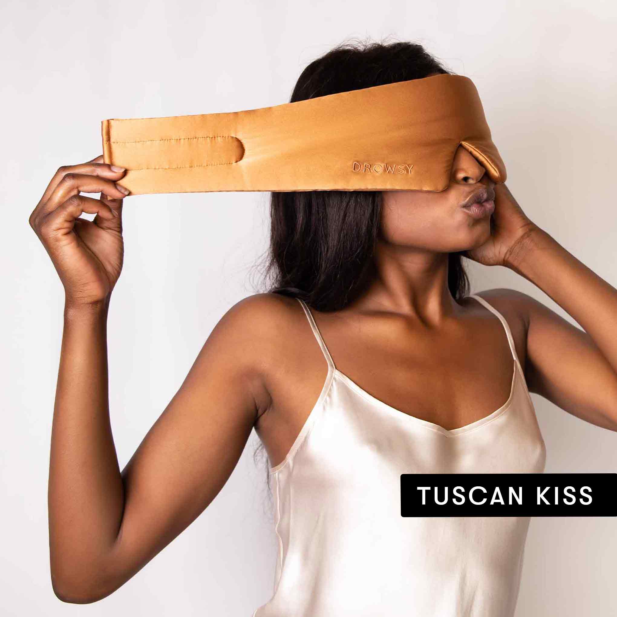 A woman in a satin camisole wears a drowsysleepco Lovers Pack silk sleep mask over her eyes, holding one side. TUSCAN KISS is displayed in a black box at the bottom right.