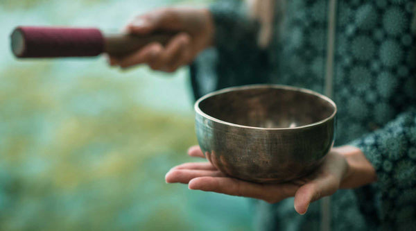 Copper meditation bowl with wooden stick being held in a hand.