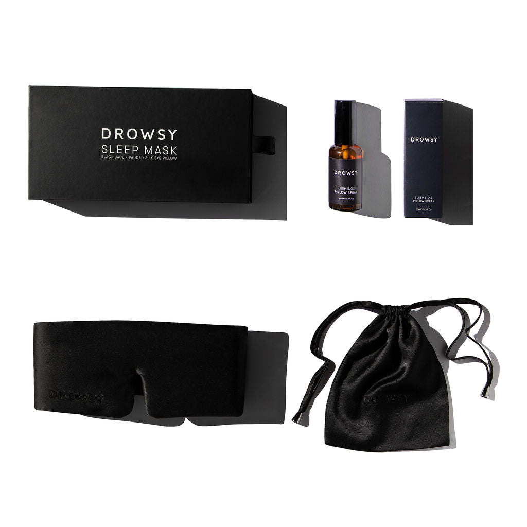 Flat lay photo of black boxes and silk sleep mask with silk pouch and a pillow spray on a white background