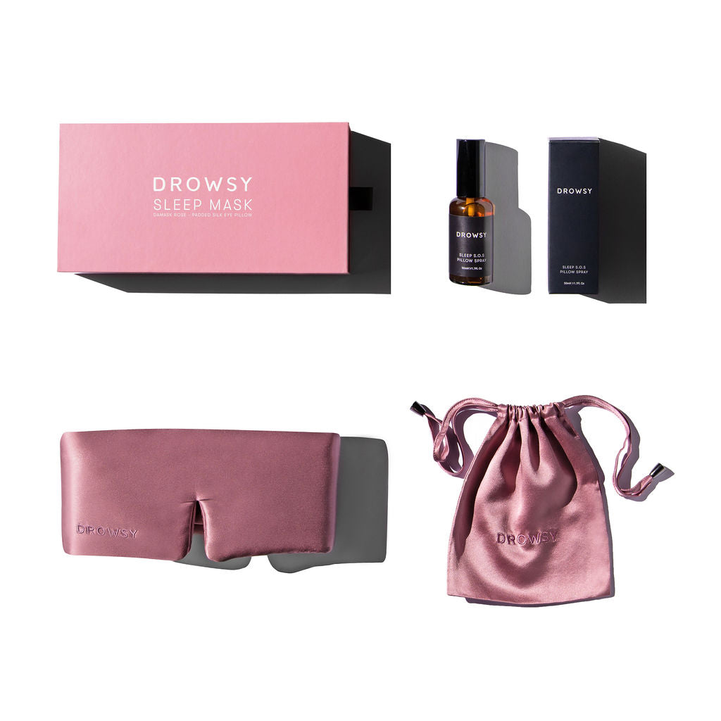 Flat lay photo of pink boxes and silk sleep mask with silk pouch and a pillow spray on a white background