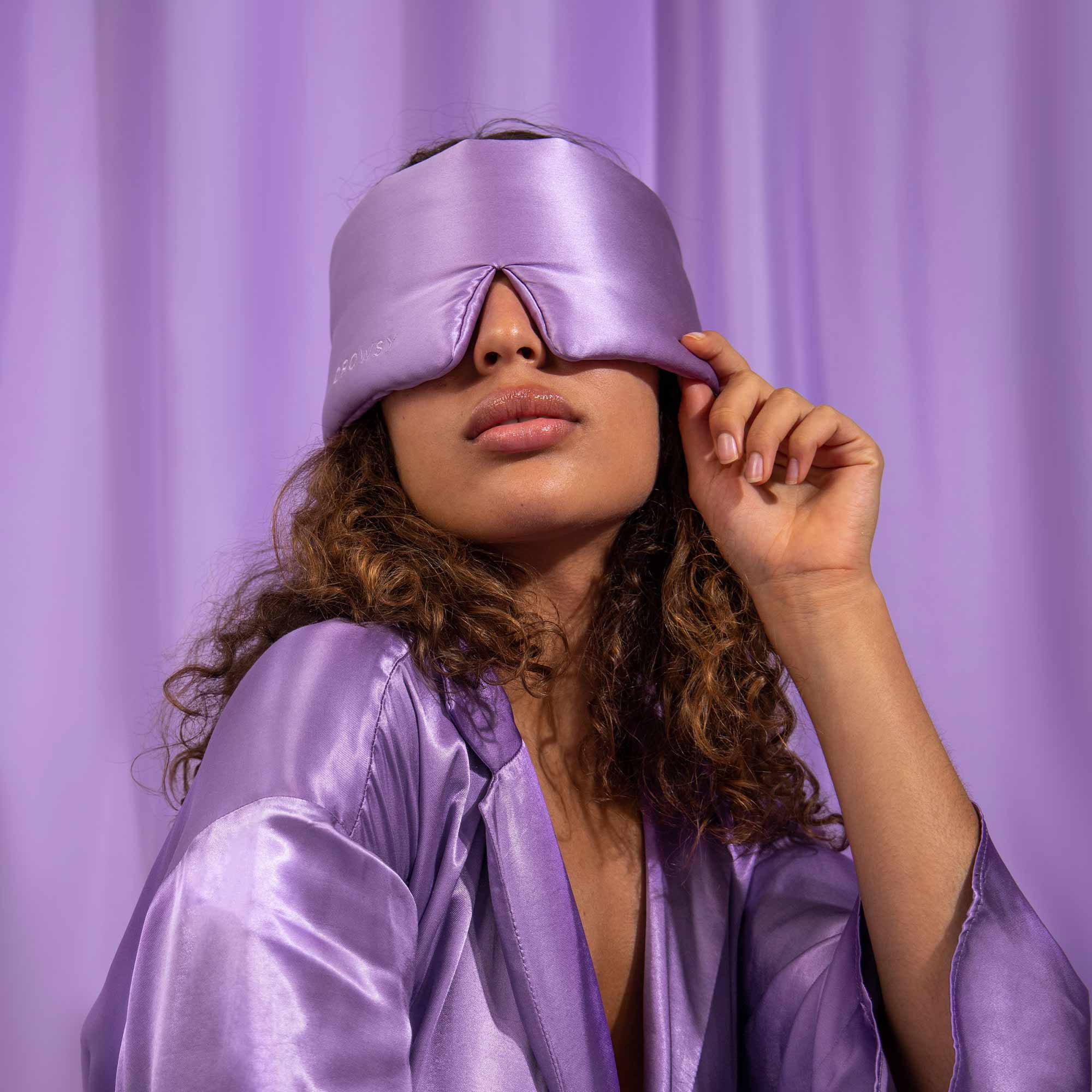 Model with Lavender coloured Drowsy sleep mask covering eyes with a purple silk backdrop