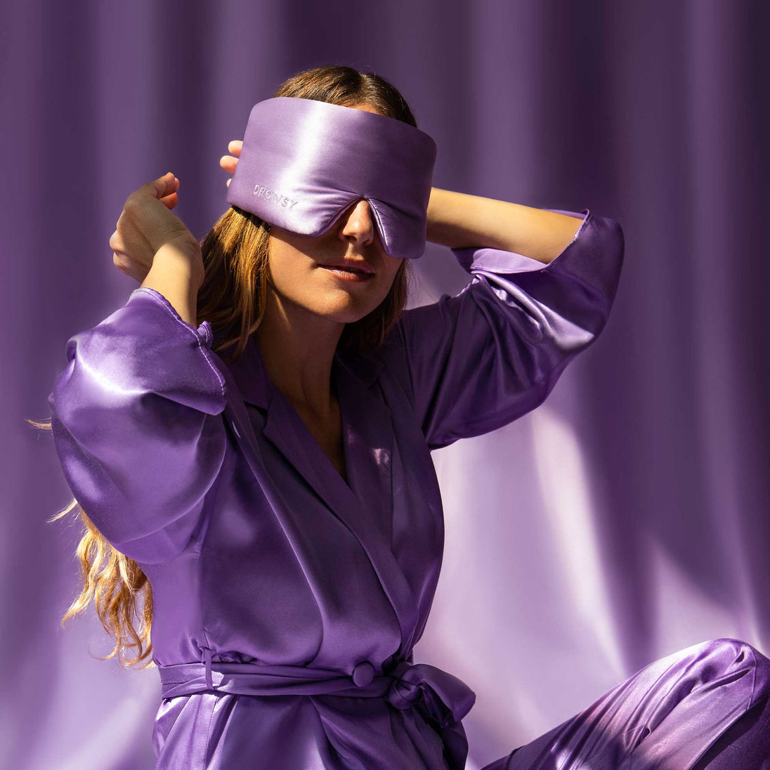 Model with Lavender coloured Drowsy sleep mask covering eyes with a purple silk backdrop