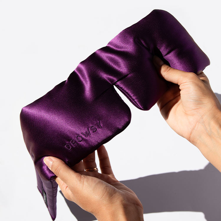 Hands squeezing purple coloured silk sleep mask with a white background