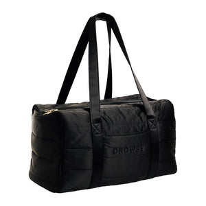 The Drowsy Silk Weekender - Black Jade by Drowsy is a quilted black duffel bag featuring two long handles, a zipper closure, and the word “DROWSY” embroidered on the side—perfect as a stylish weekend bag for your next getaway.