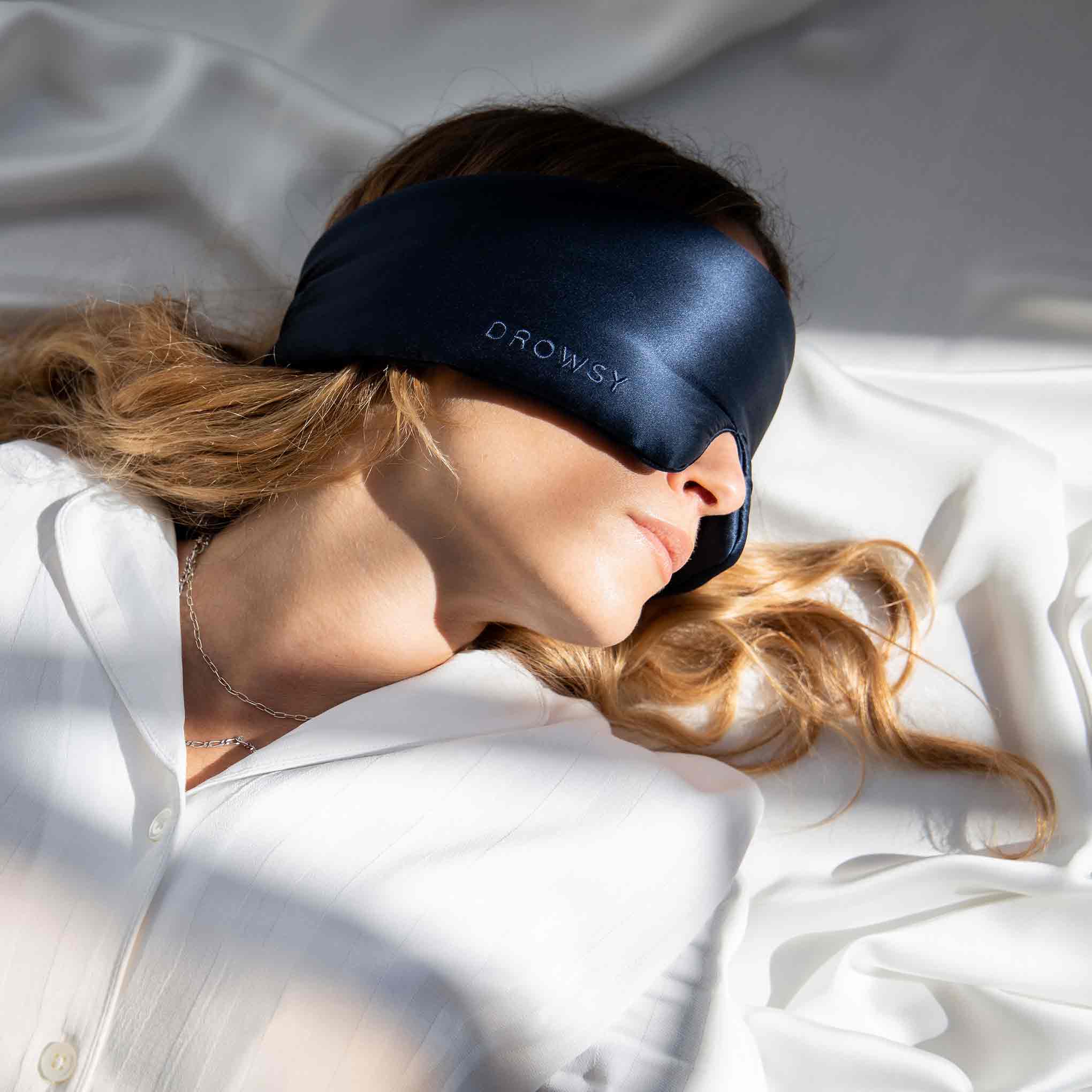 Model sleeping in the sunlight with a Drowsy silk sleep mask covering her eyes