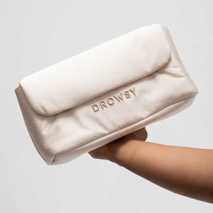 A hand holds the Drowsy Silk Necessaire in Dusty Gold by Drowsy, a soft, cream-colored pouch with gold DROWSY embroidery—an elegant accessory to elevate your beauty or skincare routine against a plain backdrop.