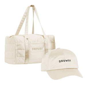 The Drowsy Roadtrip bundle in Dusty Gold includes a cream duffel bag and matching cap, both embroidered with "DROWSY" in black—ideal for stylish travel hair care and effortless protection, shown on a plain white background.