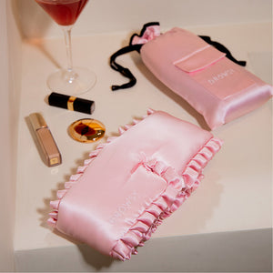 The Sleep and the City - Powder Pink Sleep Mask + Pouch by drowsysleepco features a pink silk mask with ruffled edges and ‘DROWSY’ embroidery, plus a satin pouch—perfect for blackout sleep and enhanced skincare.