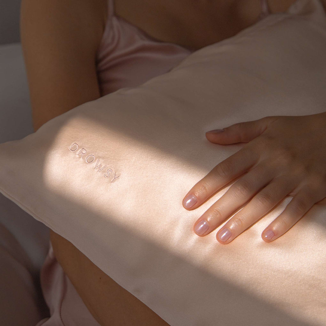 Hands of a model holding a pastel pink coloured Drowsy silk pillowcase