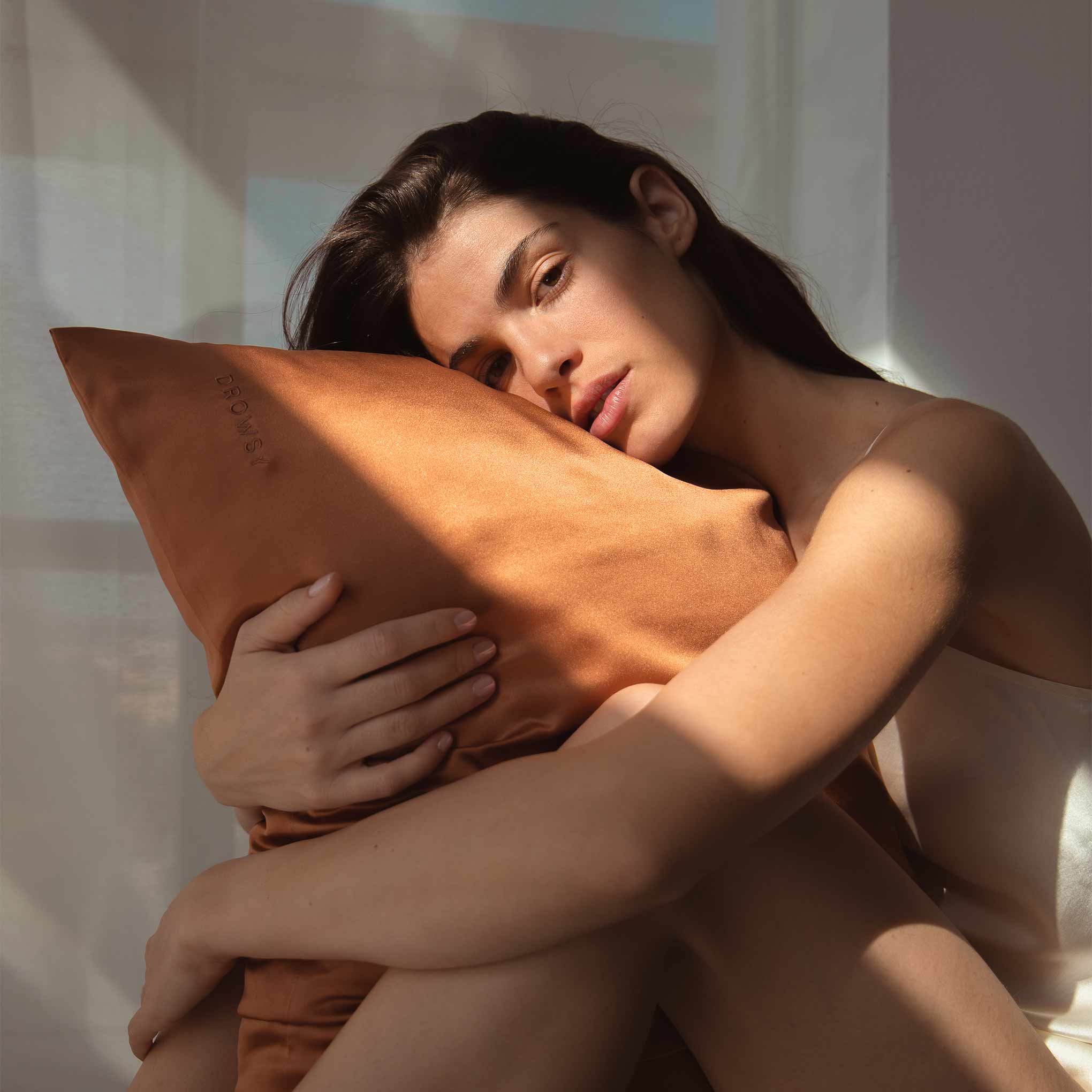 Female model hugging terracotta coloured Drowsy silk pillowcase