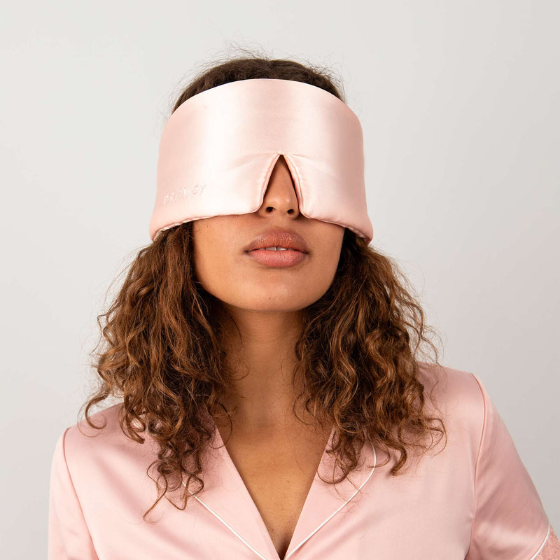 Model wearing Drowsy Sunset Pink Silk Sleep Mask over eyes against a white backdrop