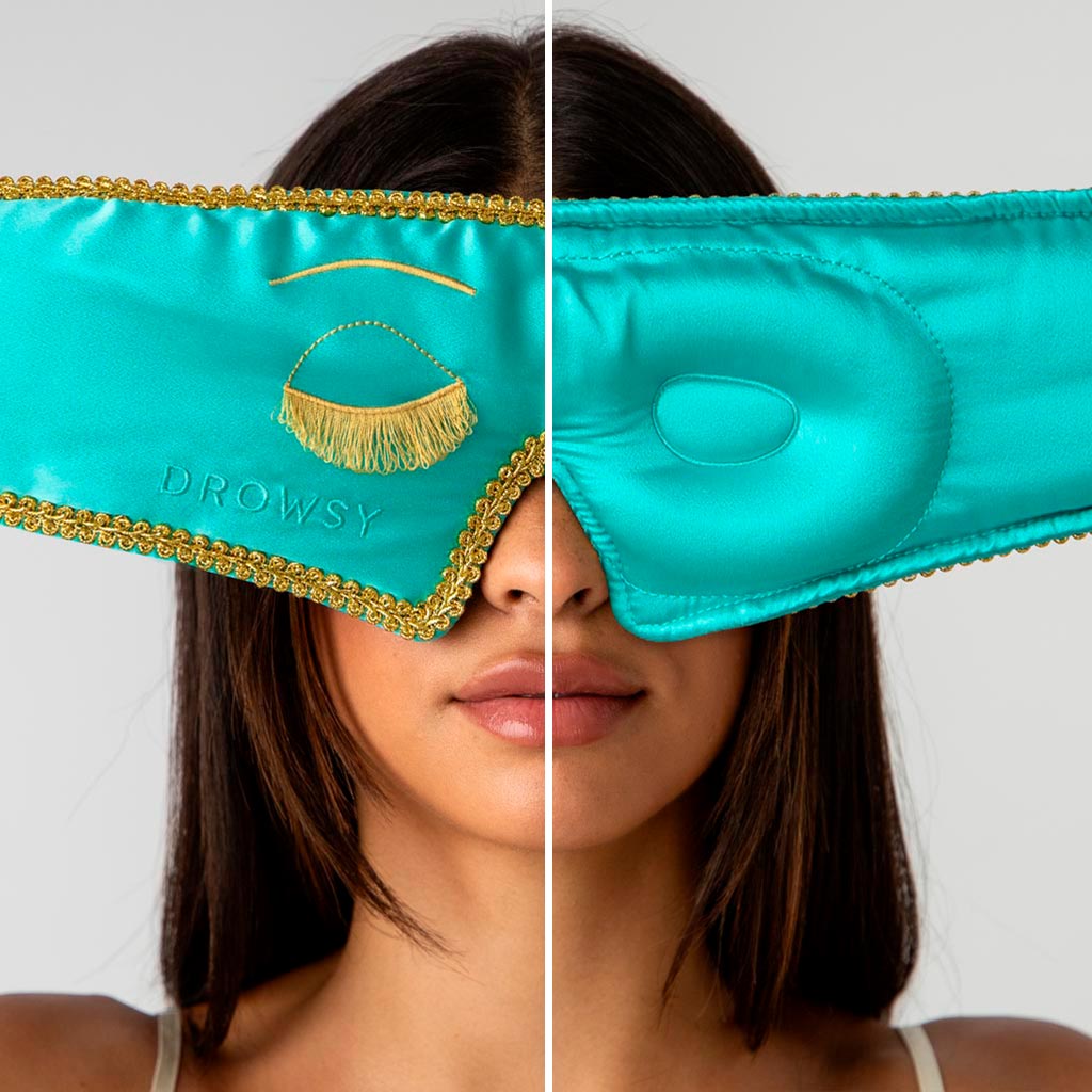 A woman with straight brown hair wears drowsysleepco’s Breakfast at Drowsy - Eyelash Protecting Mask: turquoise, with gold trim, embroidery, and “DROWSY” on the left side; the right side is plain with a raised circular area.