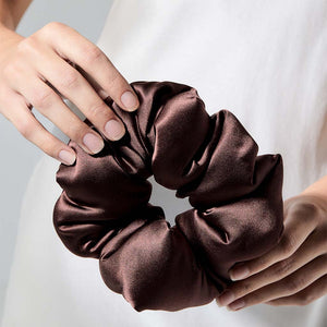 A person holds the drowsysleepco Cocoa Glow - Padded Scrunchie with both hands, displaying neatly manicured nails and wearing a white garment.