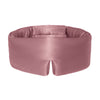 A woman adjusts a silky, mauve Sensual Sleep Bundle - Damask Rose sleep mask by drowsysleepco over her eyes, against a plain white background.