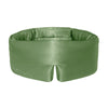 A woman with long dark hair rests on a white bed, wearing the drowsysleepco Pistachio Green silk sleep mask on her forehead and gazing calmly at the camera.