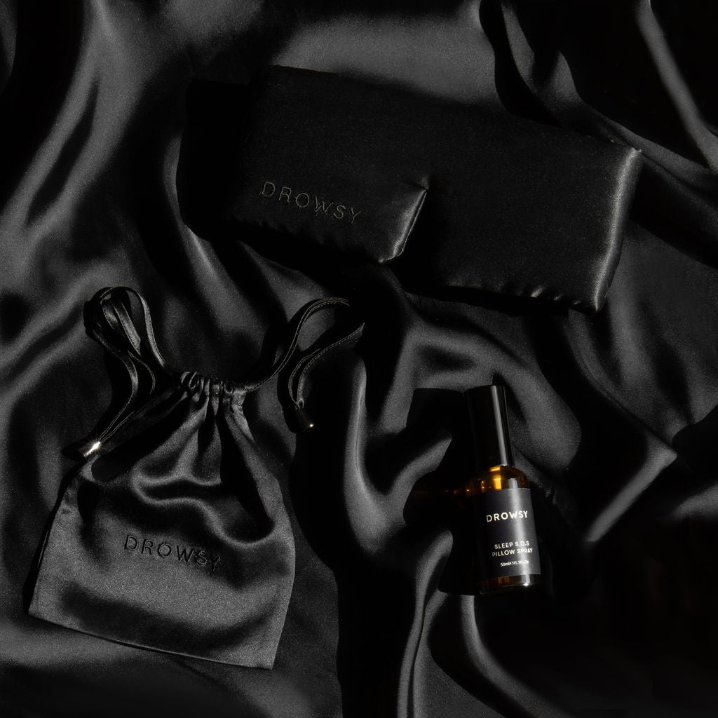 Black sleep mask, black silk pouch and pillow spray on black silk background