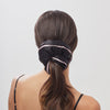 A woman with long brown hair in a low ponytail, secured with the Sleep and the City - Black Padded Scrunchie by drowsysleepco, featuring a thin light pink trim, shown from behind against a plain light background.
