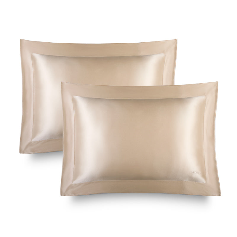 Two champagne gold, rectangular Hyalo Pillowcases by us.drowsysleepco with a smooth, lustrous finish are displayed side by side against a white background. Each pillowcase features a wide border and a subtle logo in the lower right corner, offering an elegant touch while supporting overnight hydration for your skin.
