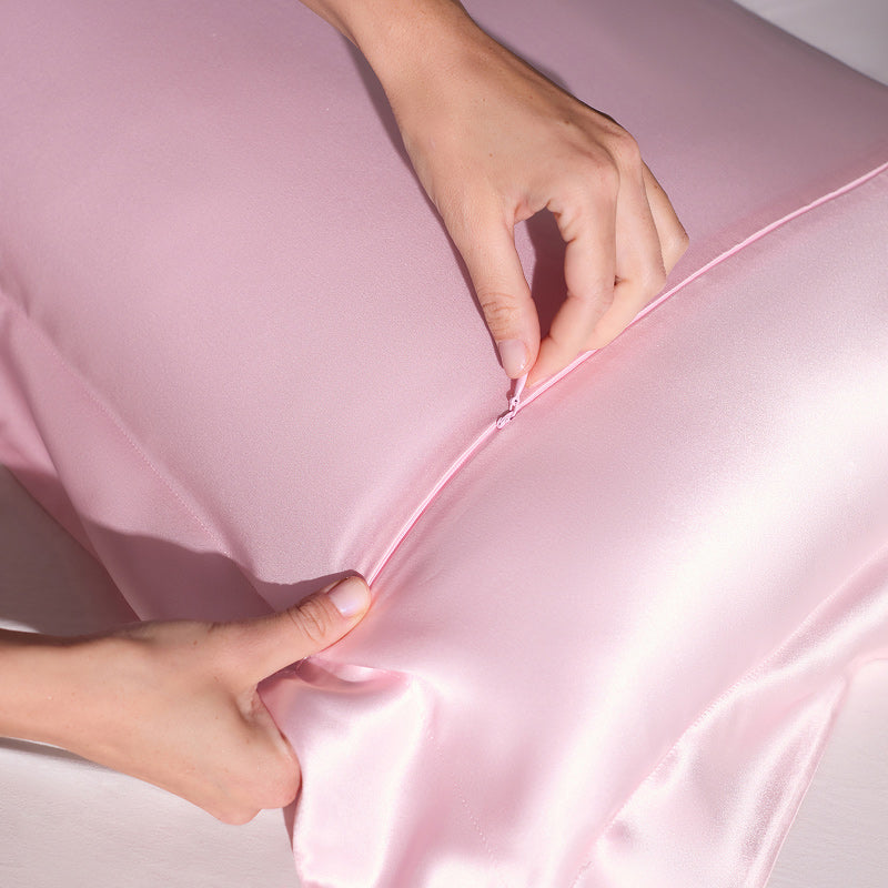 Close-up of hands zipping the us.drowsysleepco Hyalo Pillowcase in Petal Pink onto a pillow.
