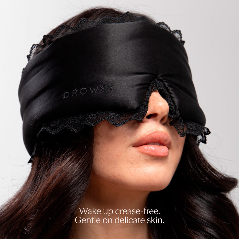 A woman wears the Paris Love Story - Black Jade Sleep Mask by drowsysleepco, crafted from black silk with lace trim and “DROWSY” embroidered on it. Text below: Wake up crease-free. Gentle on delicate skin for true beauty sleep.
