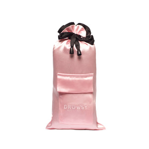 The Sleep and the City Silk Carry Pouch by drowsysleepco is a pink satin drawstring bag with a black ribbon, front pocket, and DROWSY embroidery—an elegant, luxury sleep mask pouch standing upright against a white background.