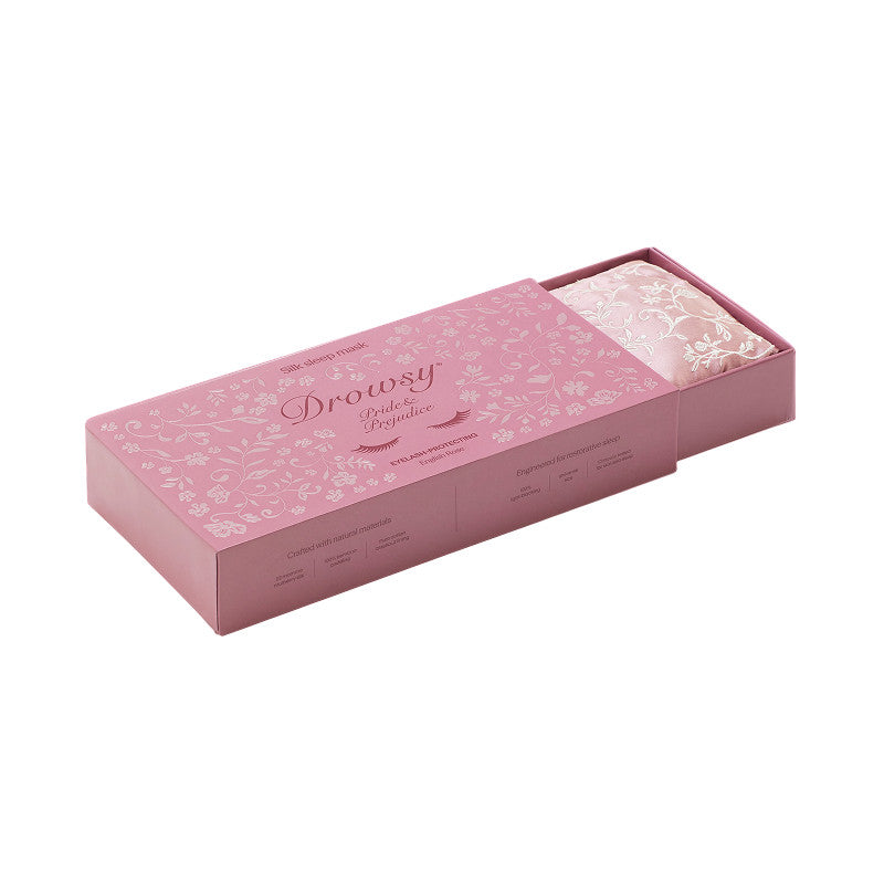 A pink rectangular box with floral patterns containing the Pride & Prejudice - Sage + English Rose Eyelash Protecting Masks, a folded, patterned silk sleep mask.