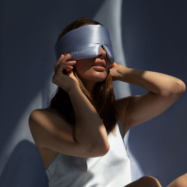 Model blocking out light from her eyes with a baby blue coloured silk sleep mask from Drowsy